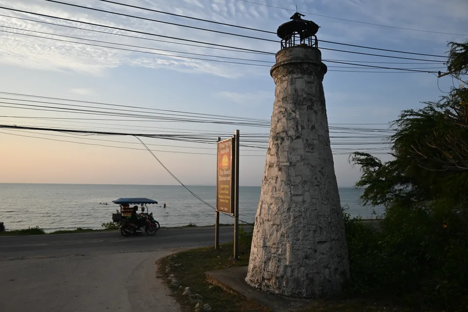 An old stone lighthouse beside the coastal road and sea in Bang Saray.
